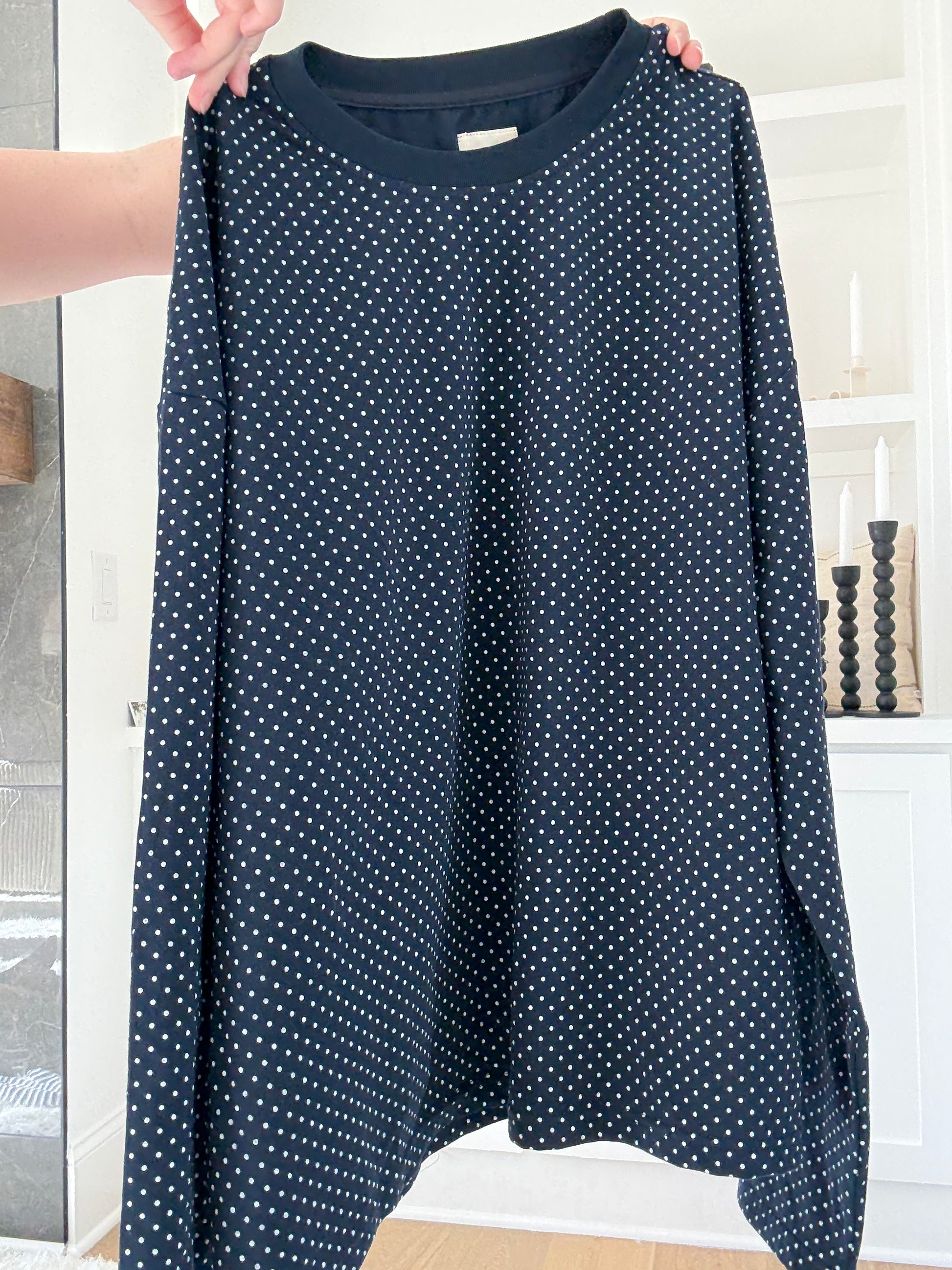 Navy blue long-sleeve shirt with white polka dots held by a person indoors.