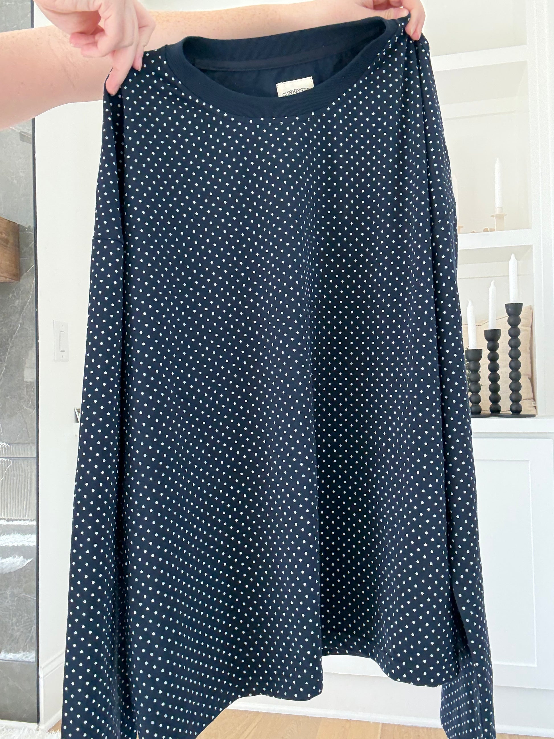Navy blue dress with white polka dots held by a person indoors.