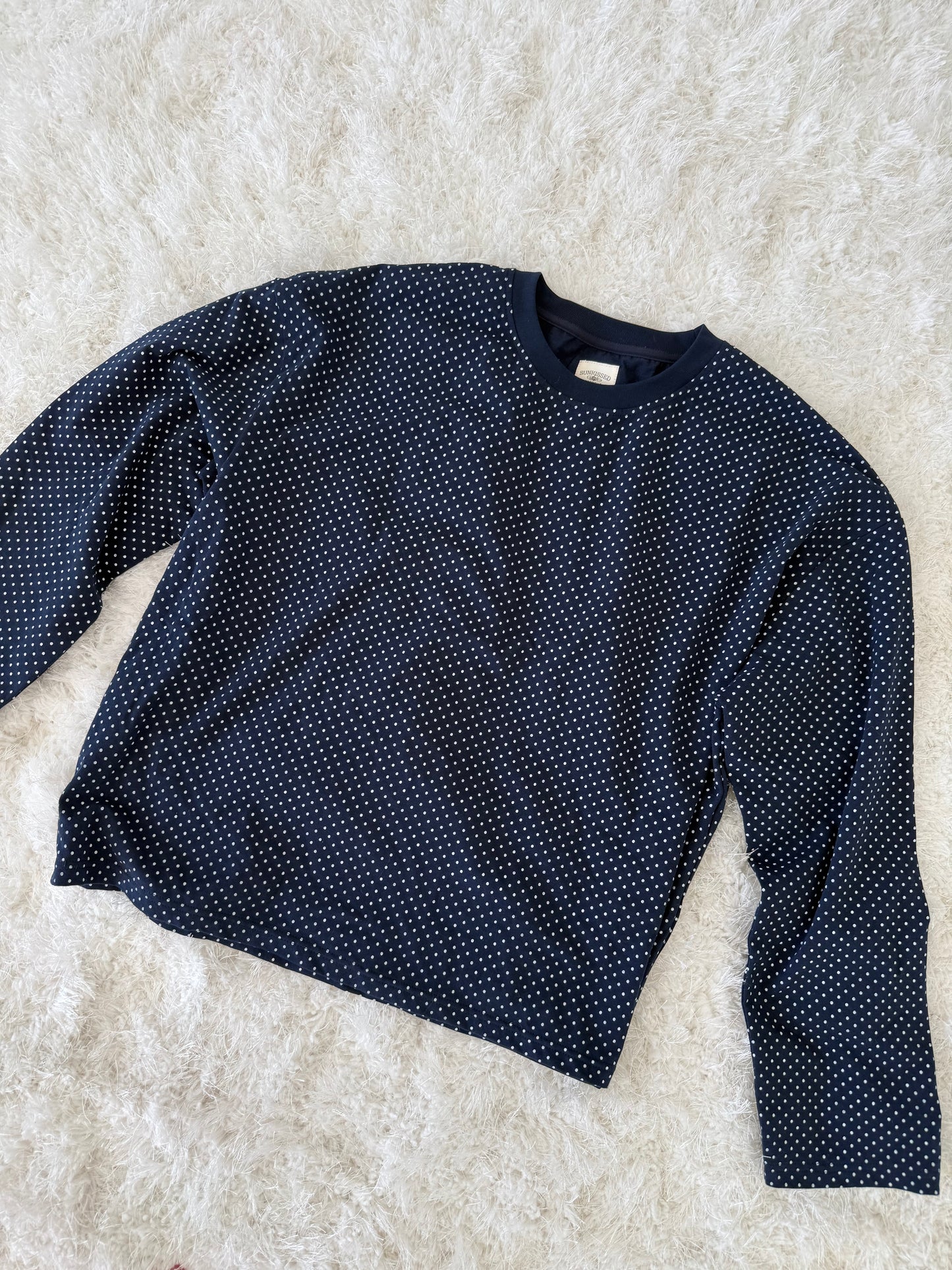 Navy blue long-sleeve shirt with white polka dots on a light beige surface
